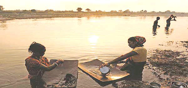 सोना निकालने के लिए नदी की मिट्री छानती आदिवासी महिलाएं 